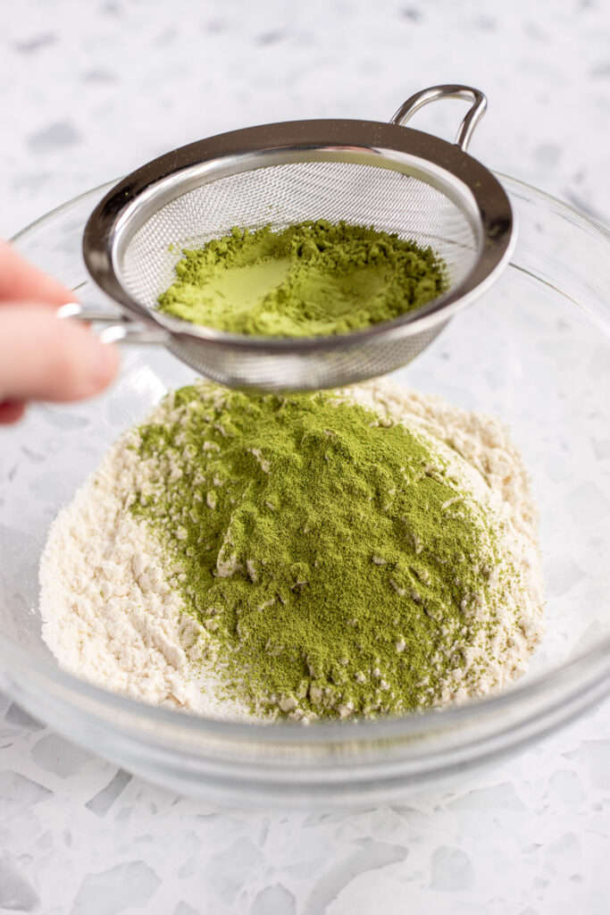 Hand sifting matcha powder into a bowl of flour for making matcha sponge cake.