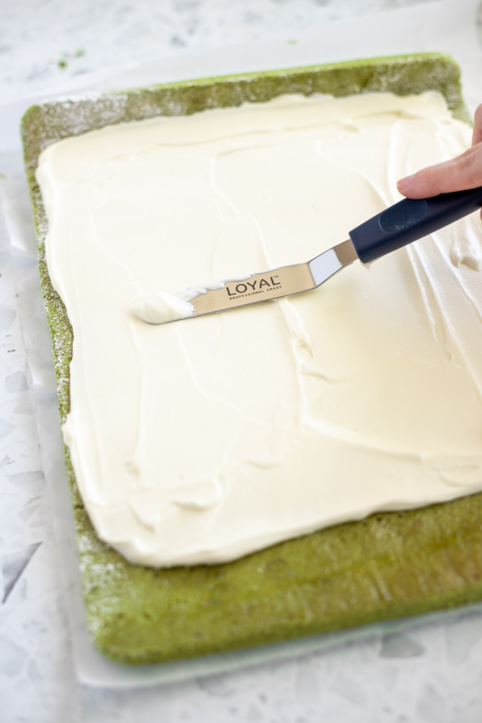 Spreading stabilised cream onto unrolled matcha sponge with an offset spatula.