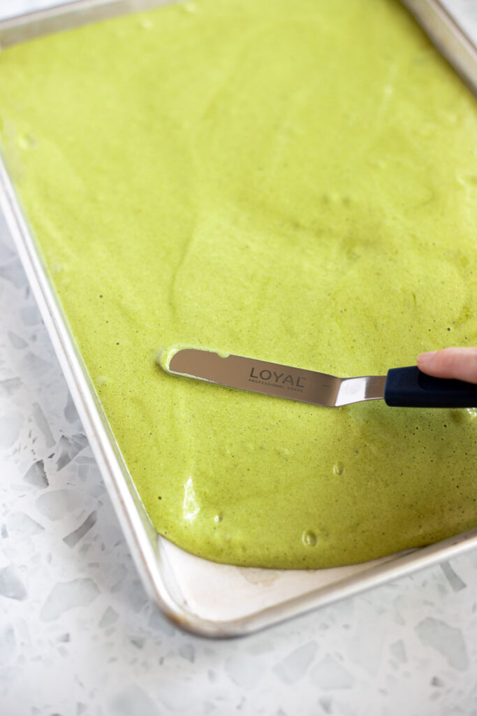Evenly smoothing green matcha batter in a lined tray using an offset spatula.