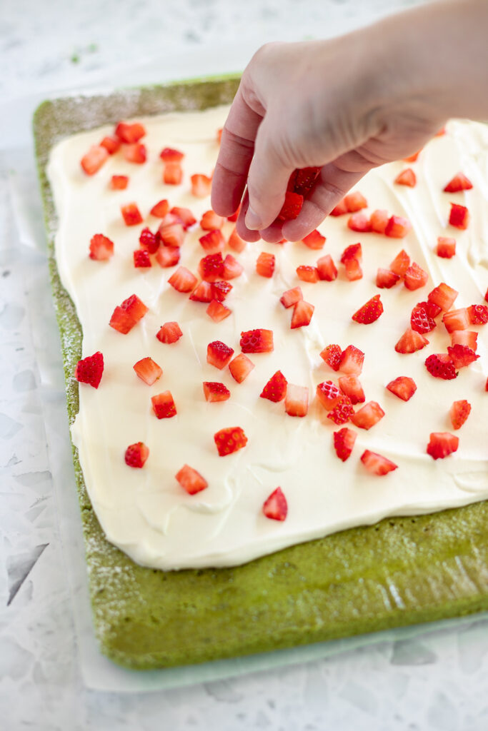 Adding chopped strawberries evenly over whipped cream filling.
