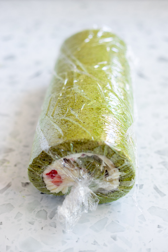 Strawberry matcha Swiss roll wrapped in cling film, ready to chill in the fridge.