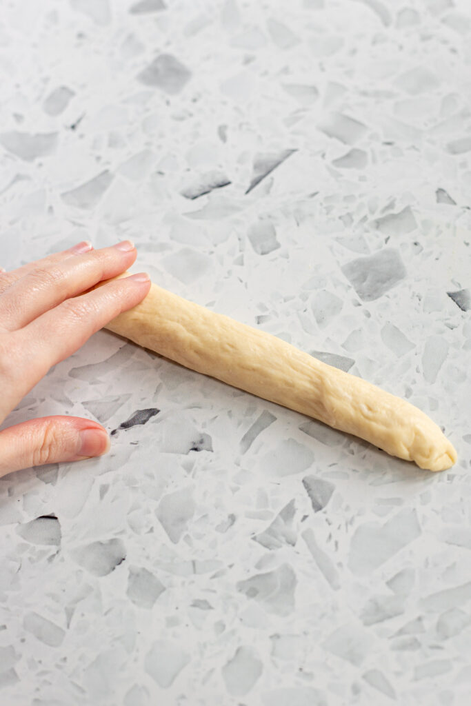 Hand shaping garlic knot dough into ropes for twisting into knots.
