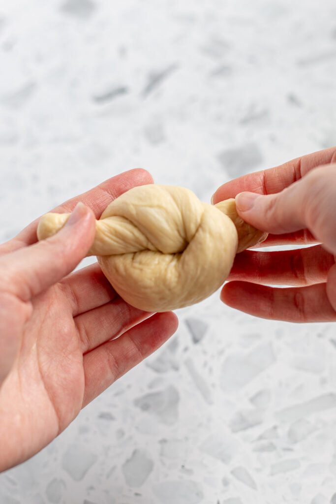 Hands pulling the ends of garlic knot dough after tying.