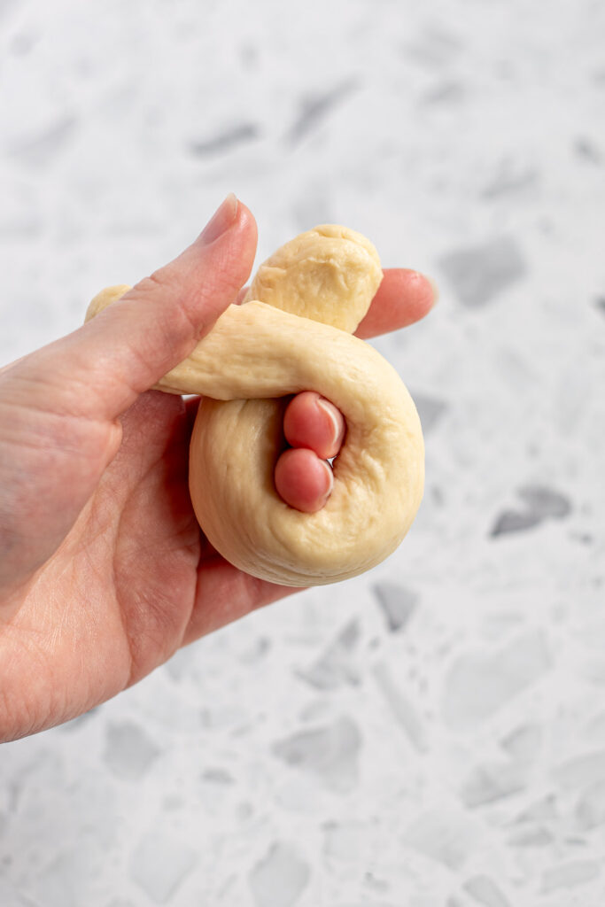 Hand holding a crossed-over dough rope, first step of tying a knot.