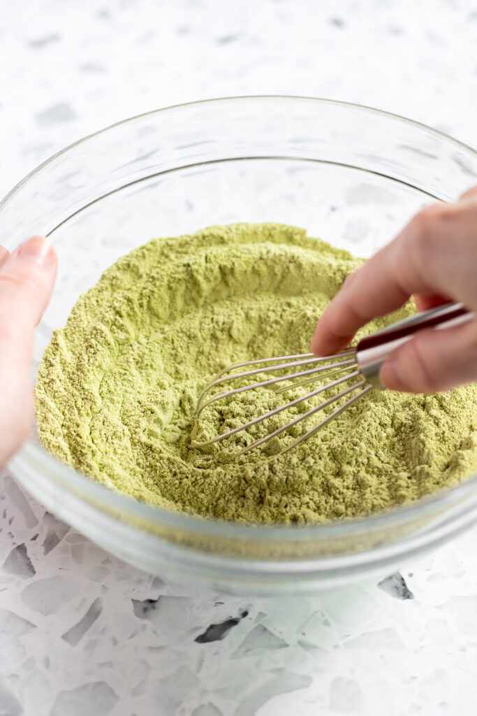 Hand whisking dry ingredients for matcha sponge cake in a bowl.