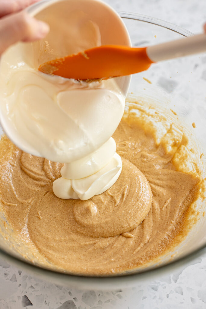 Pouring creamy greek yogurt into the blueberry coffee cake batter.