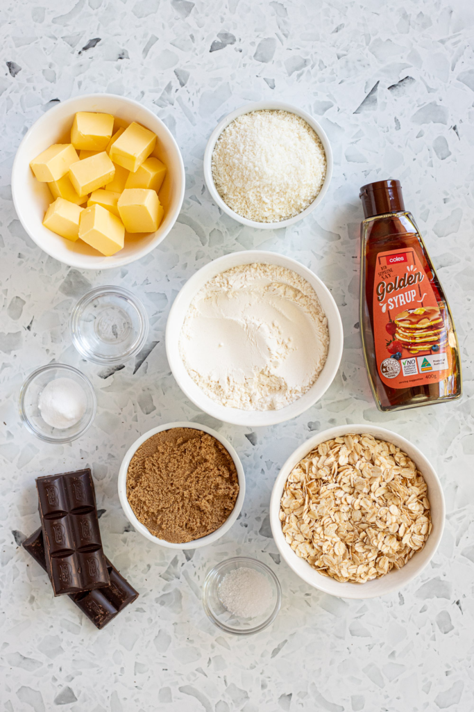 Flatlay of ingredients needed to make chewy Anzac slice such as golden syrup, oats, and coconut