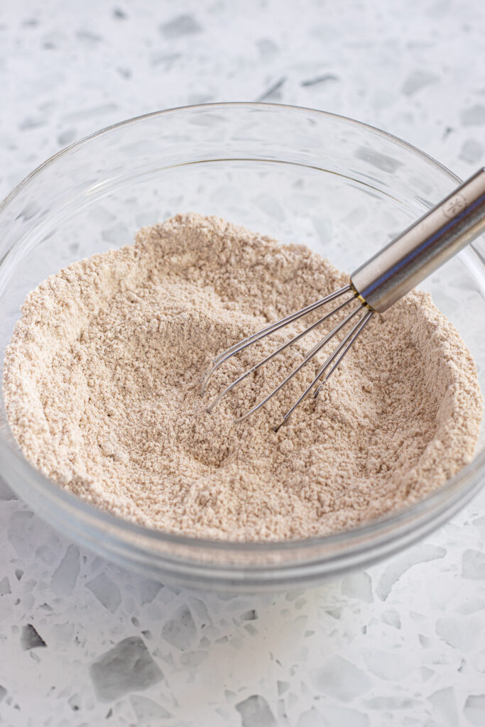 Dry ingredients for cinnamon streusel topping combined in a bowl, with a small whisk resting inside