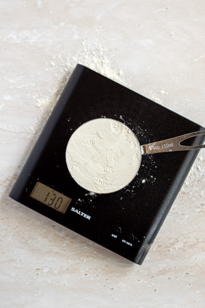 250ml measuring cup of flour measured using the spoon-and-level method, weighing 130 grams on a digital kitchen scale.