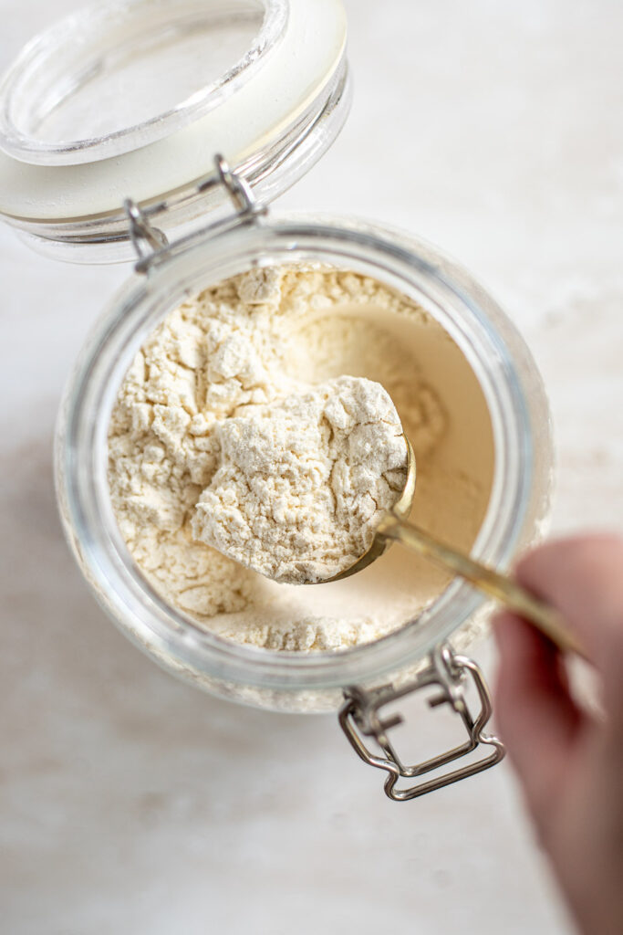 Hand fluffing flour with a spoon in a glass container.