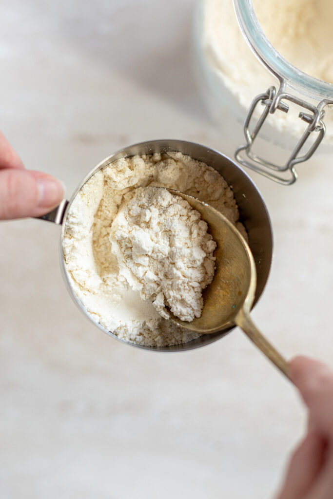 Hand spooning flour into a cup as part of the spoon-and-level method.