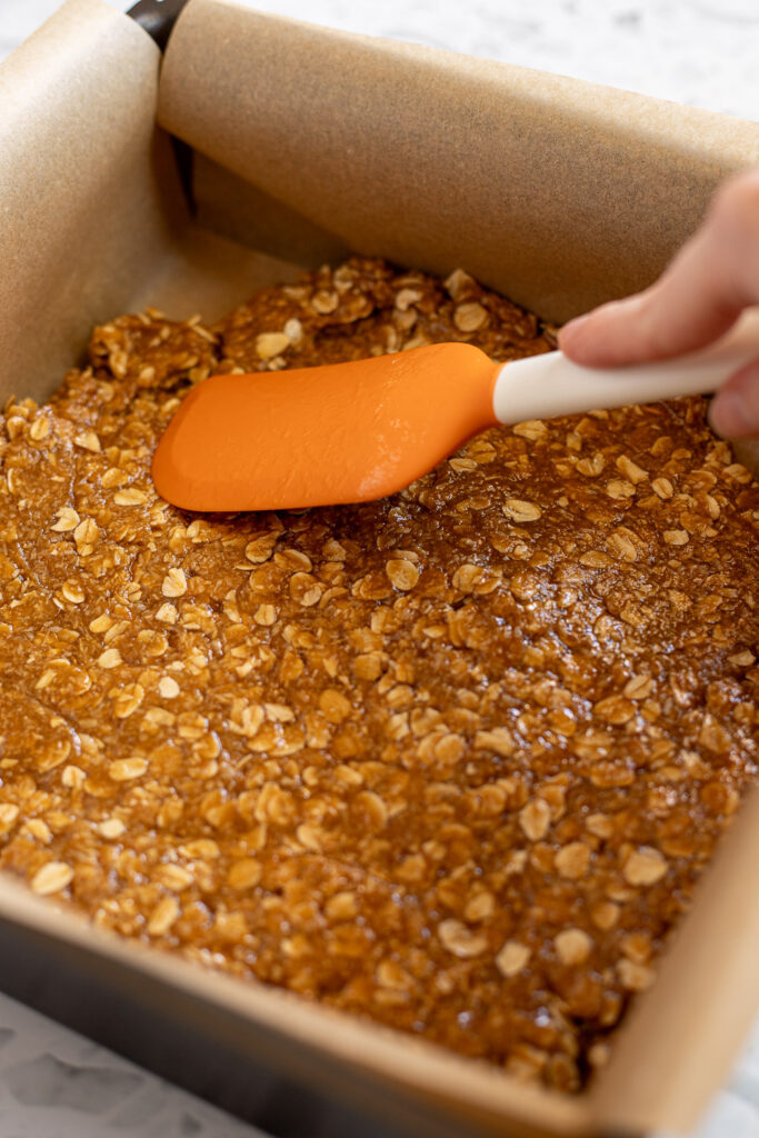 Pressing mixture into a parchment-lined square tin using a rubber spatula