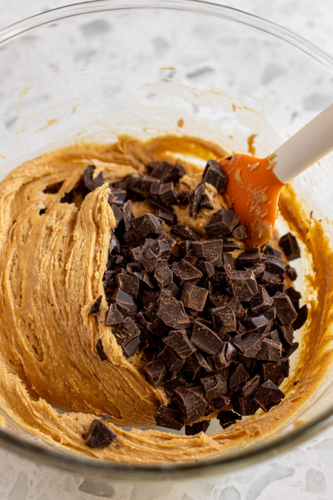 Chocolate chunks being added to peanut butter cookie dough in a mixing bowl