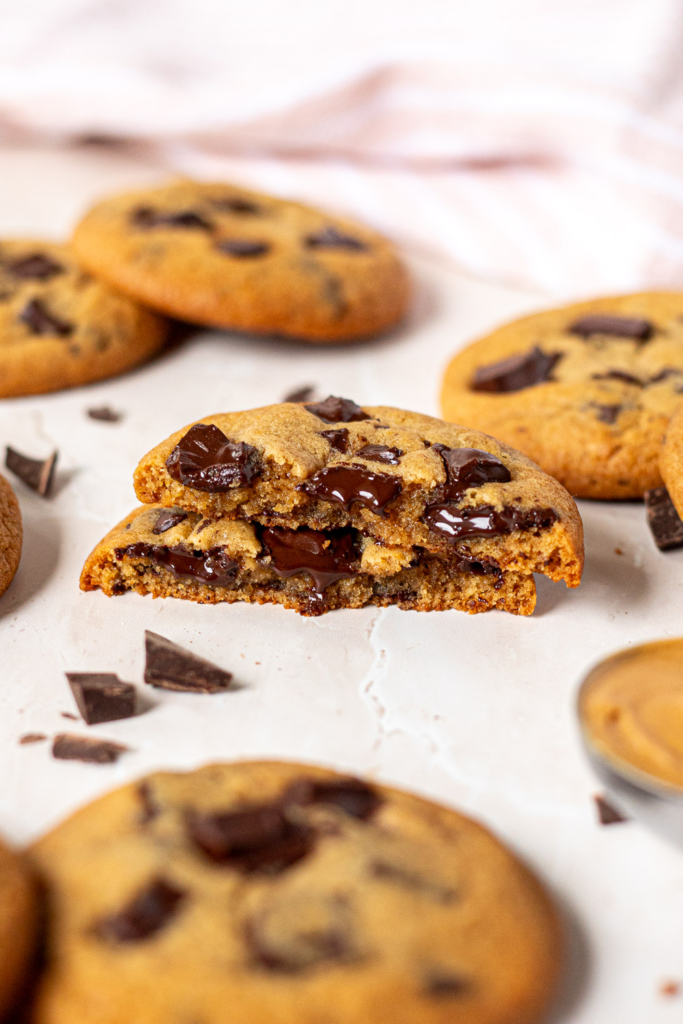 Peanut butter cookie broken in half to reveal a chewy, fudgy interior with gooey melted chocolate chunks, surrounded by more cookies and shards of dark chocolate