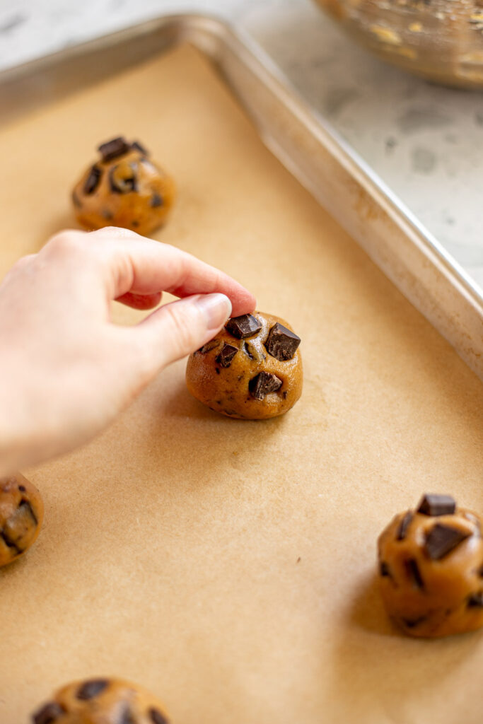 Hand pressing extra chocolate chunks into the tops of peanut butter cookie dough balls