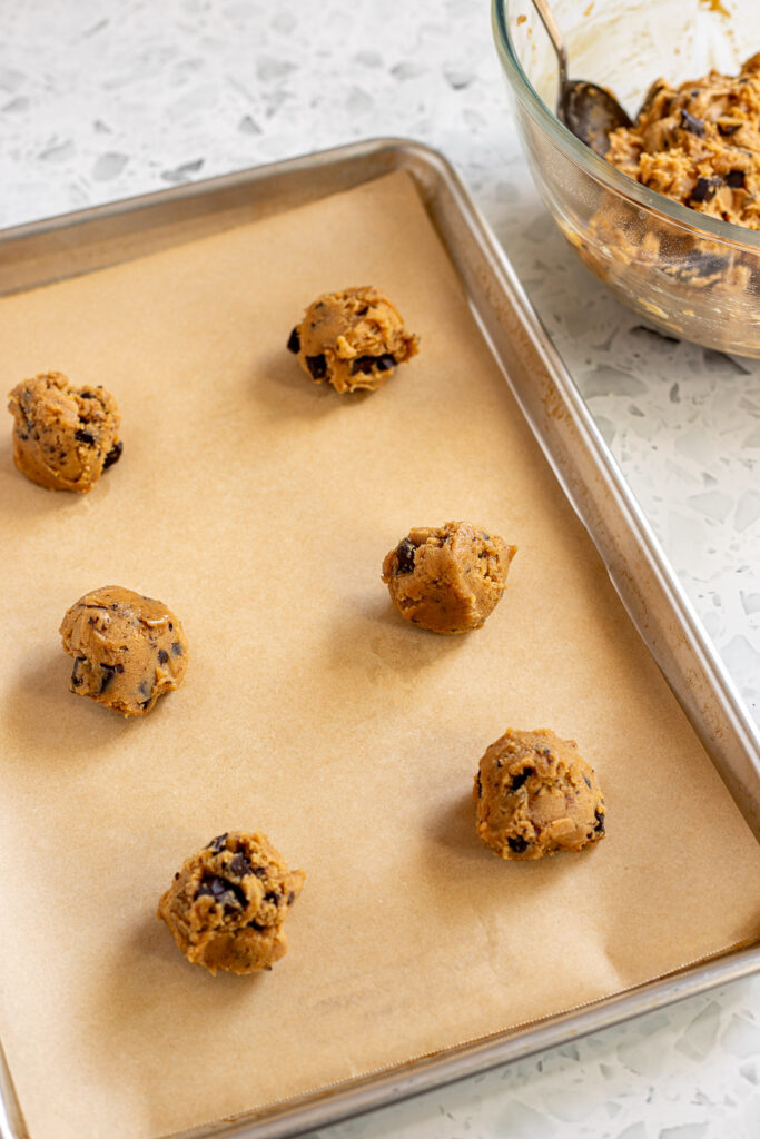 Scooped peanut butter cookie dough balls on a parchment-lined tray with a bowl of dough in the background