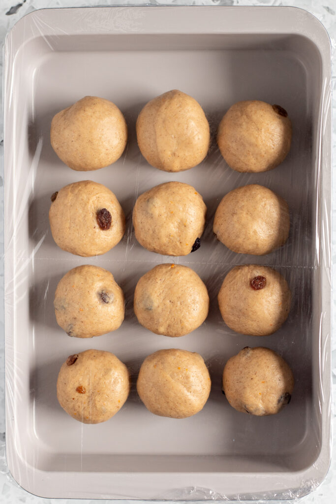 Hot cross buns in a baking tin, covered and resting for second rise
