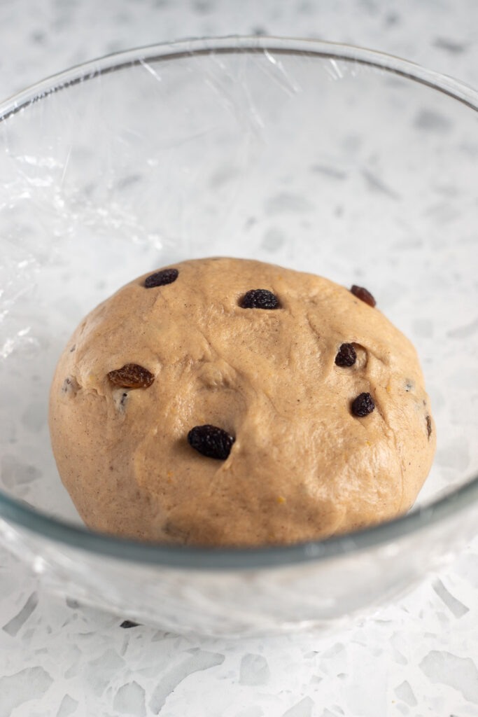 Hot cross bun dough in a greased bowl covered with cling film, ready for first rise