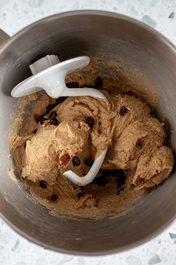 Sticky hot cross bun dough in a stand mixer bowl with a dough hook resting inside