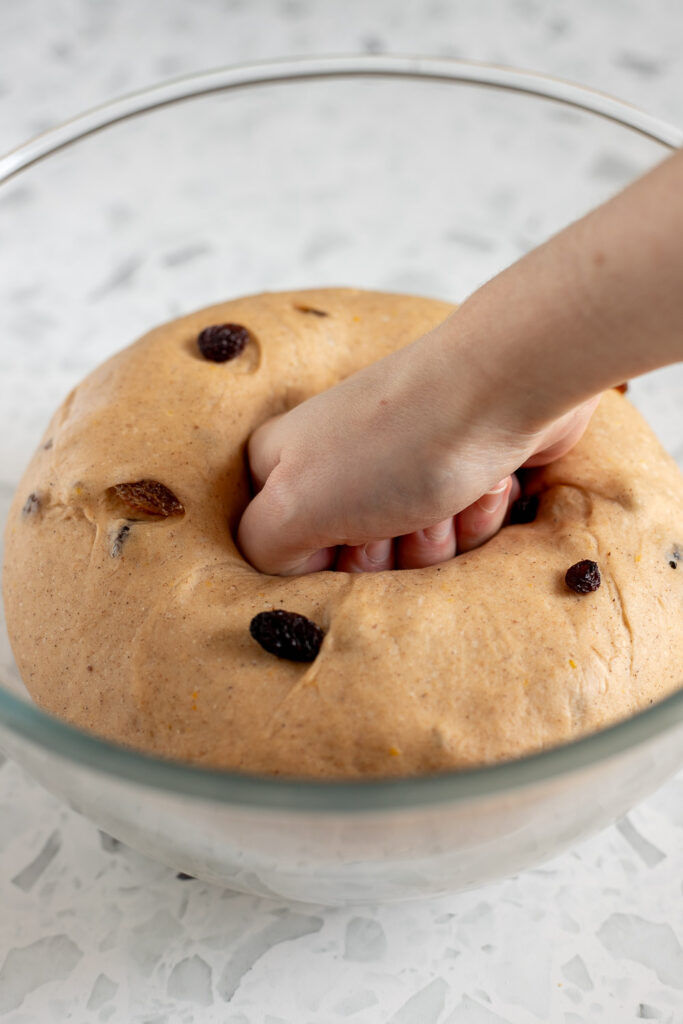 hand punching down risen dough to deflate it