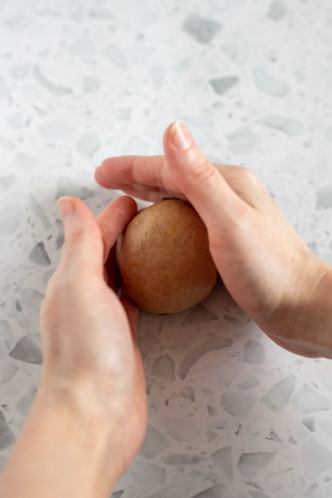 Hands rolling hot cross bun dough balls on a countertop to smooth and seal the bottom