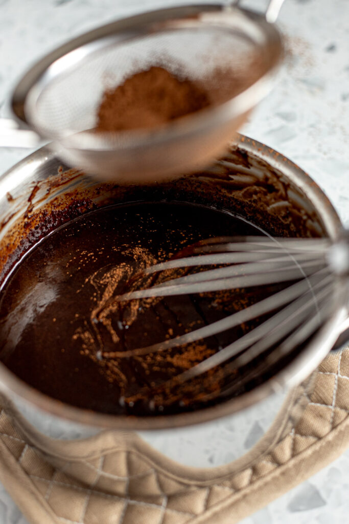Cocoa powder being sifted into warm chocolate Guinness mixture to bloom the cocoa for the cake batter