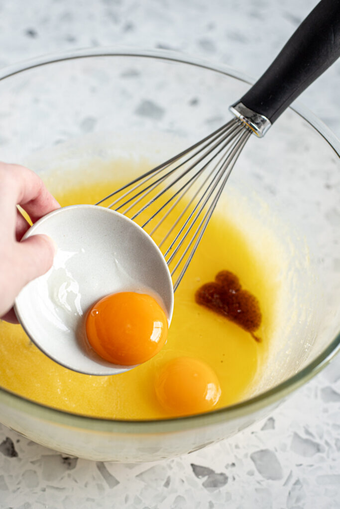 Egg yolk being added to a mixing bowl of wet ingredients such as melted butter and vanilla