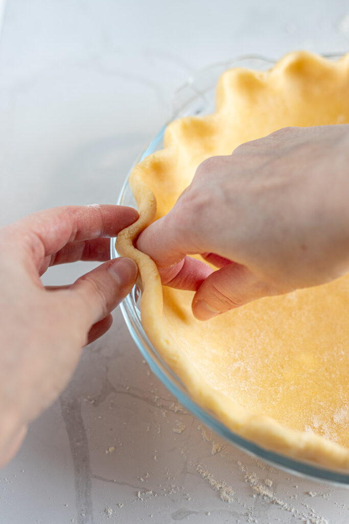 Close-up of hands fluting pie crust edges in a v-shape.