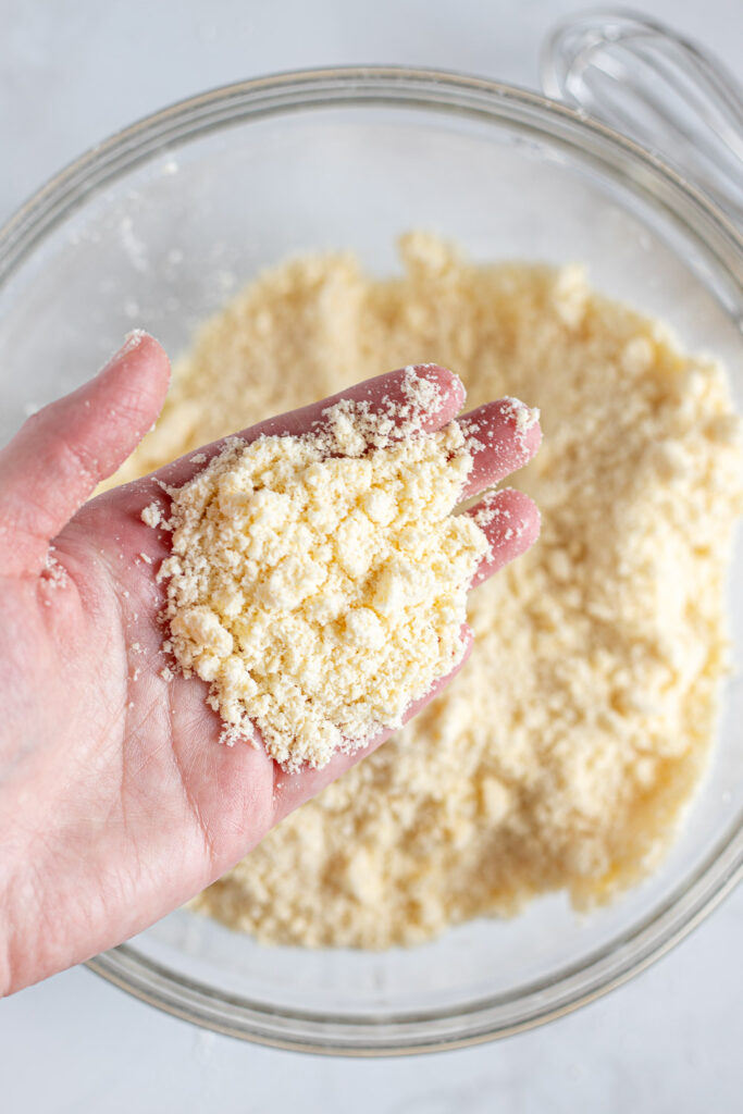 Hand showing close-up texture of butter and flour mixture, with pea-sized pieces and fine crumbs.