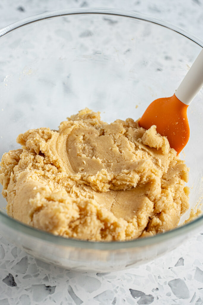 Cookie dough in a mixing bowl with a rubber spatula inside, showing a soft and thick texture