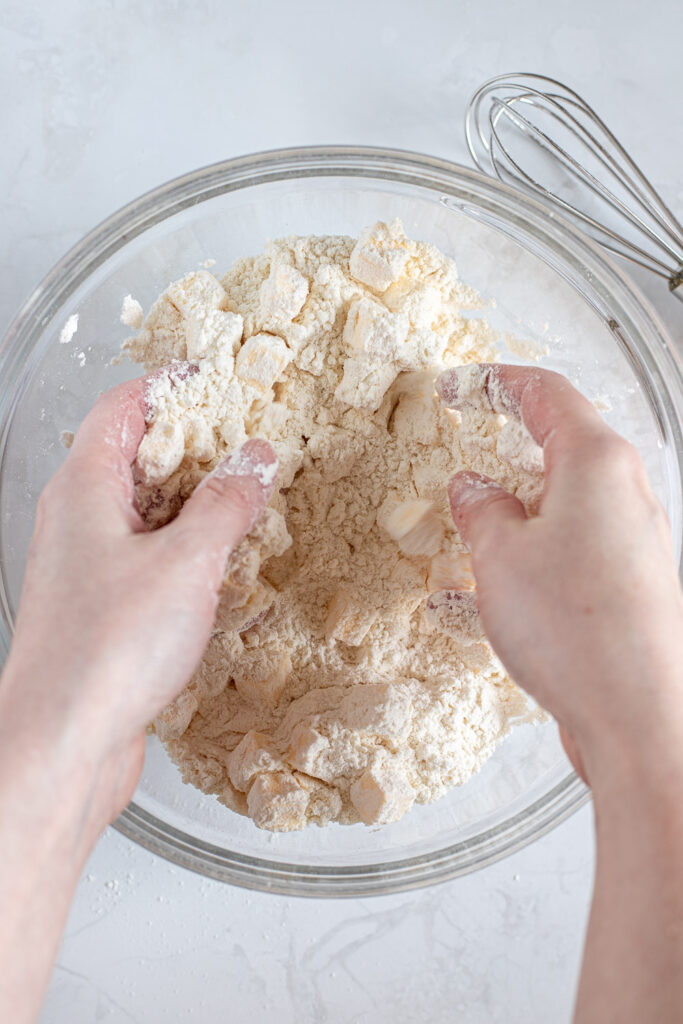 Hands tossing cold cubed butter into flour mixture.
