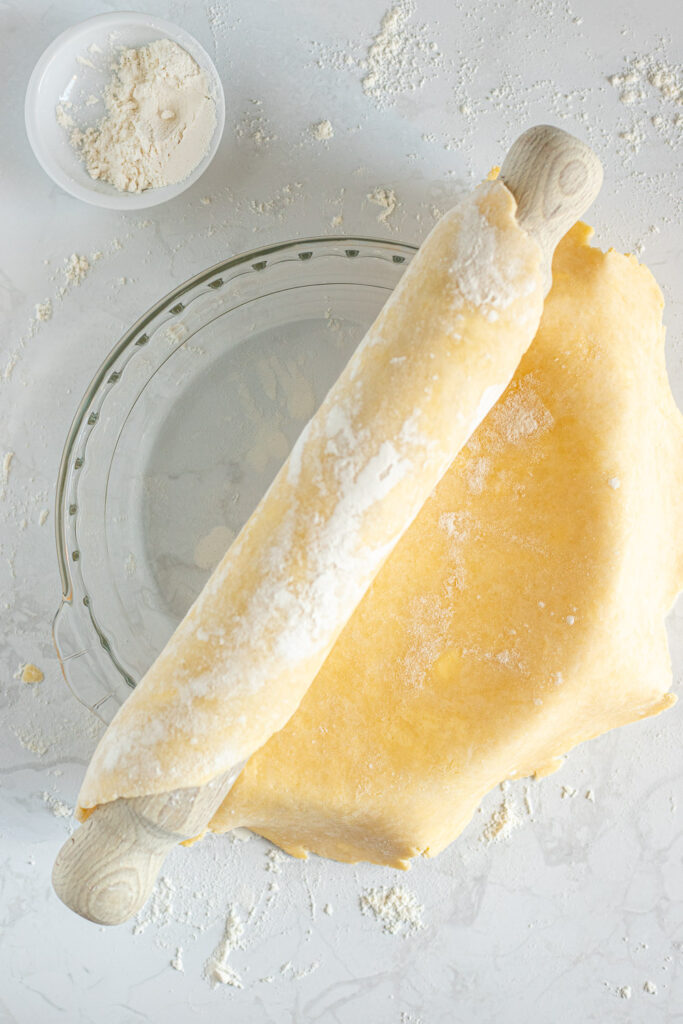 Pie crust being unrolled from a rolling pin onto a glass pie dish.