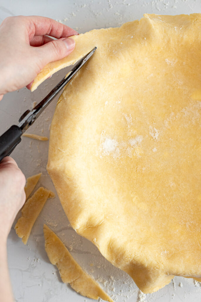 Using scissors to trim edges of pie crust.