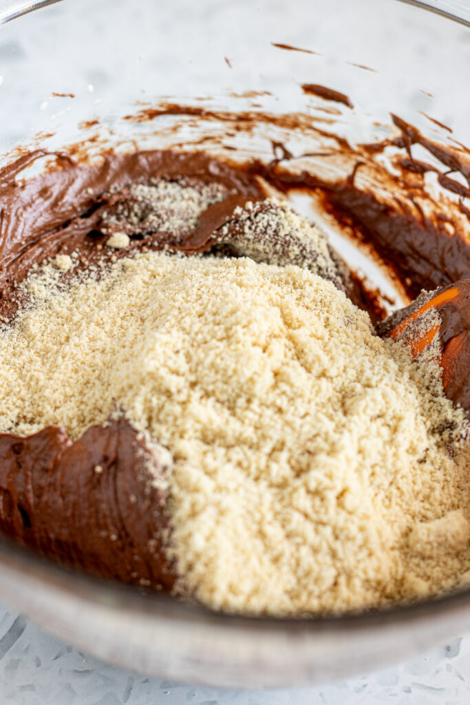 Almond meal added to a bowl of flourless chocolate brownie batter, ready to be mixed.