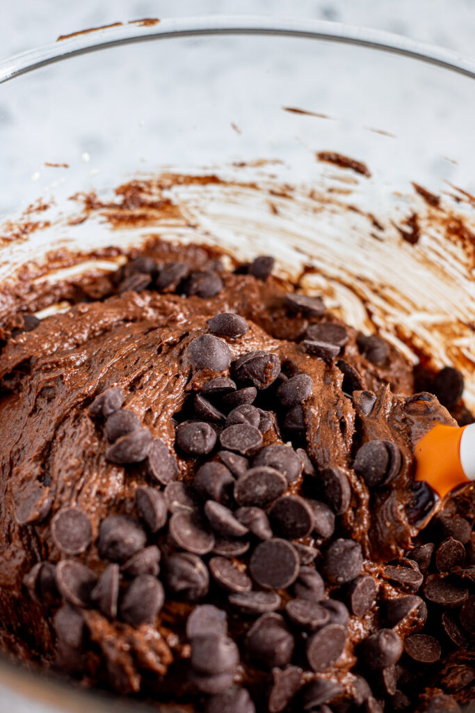 Folding chocolate chips into the brownie batter with a spatula.