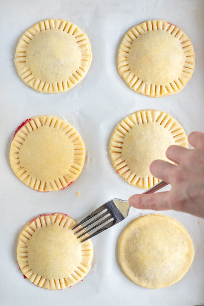 Hand crimping the edges of the hand pies with a metal fork.