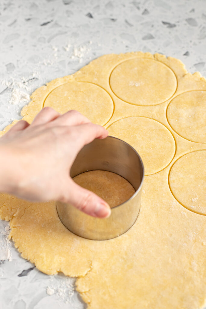 Hand cutting rounds from rolled pie dough using a circular pastry cutter.