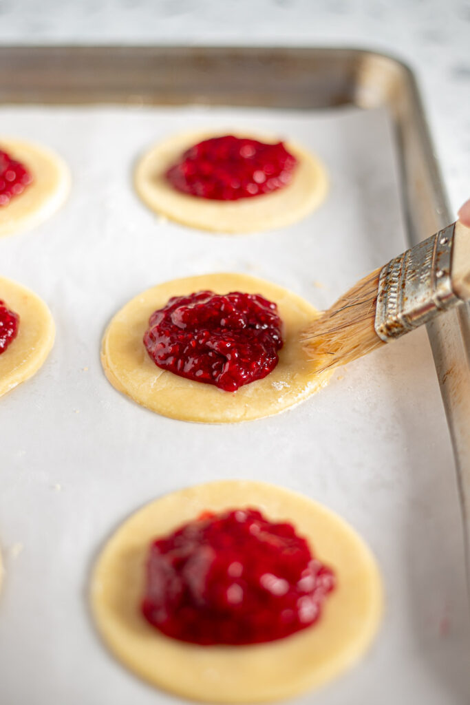 Brushing egg wash around the edges of pie dough before adding the top crusts.
