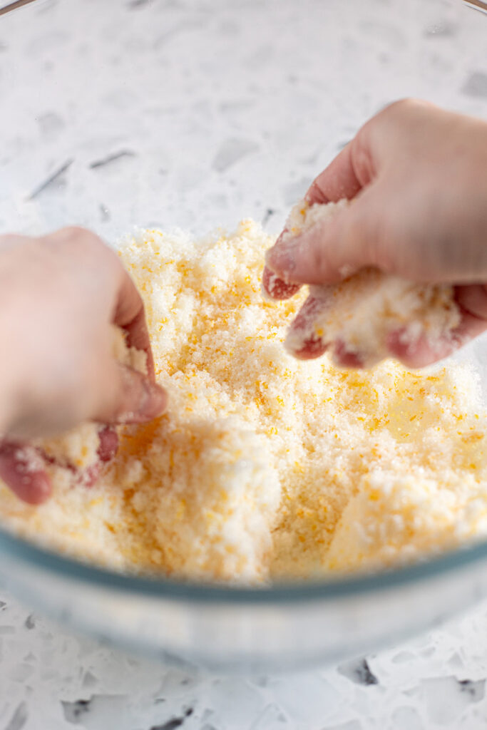 Hands rubbing fresh orange zest into sugar to release the citrus oils.