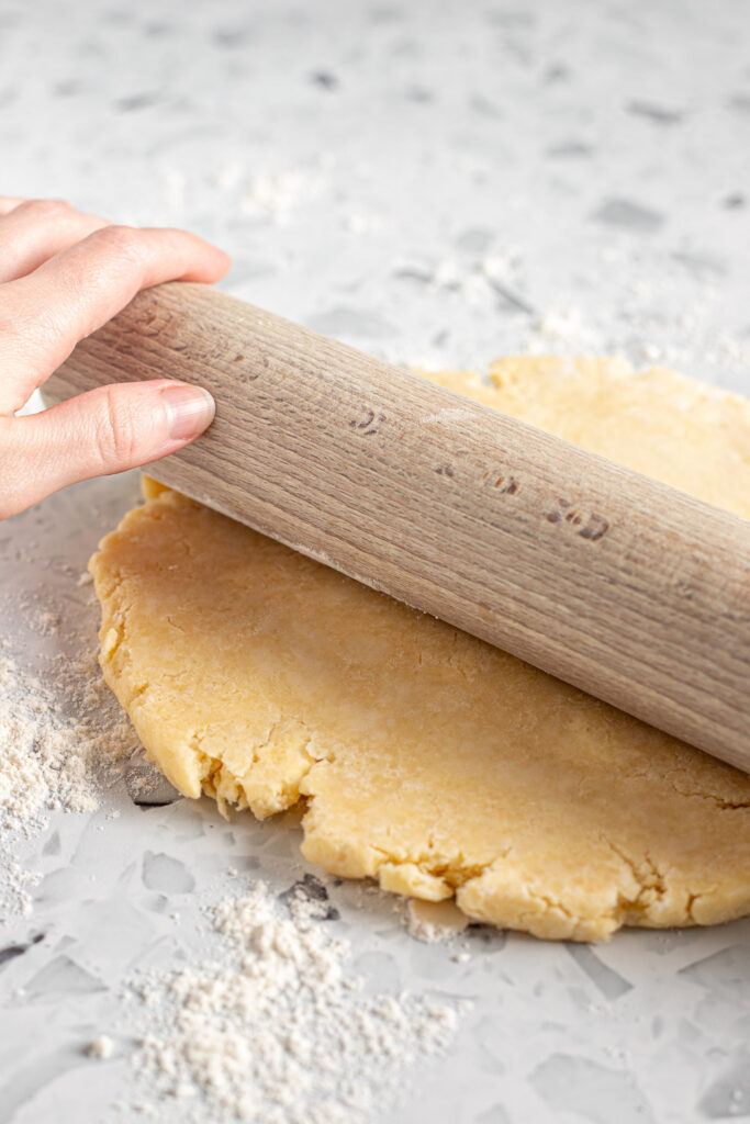 Hand rolling out homemade pie crust with a wooden rolling pin on a floured surface.