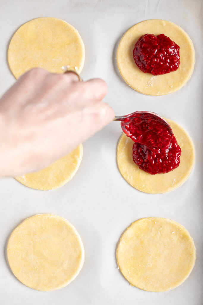Hand spooning raspberry filling onto cut circles of pie dough.