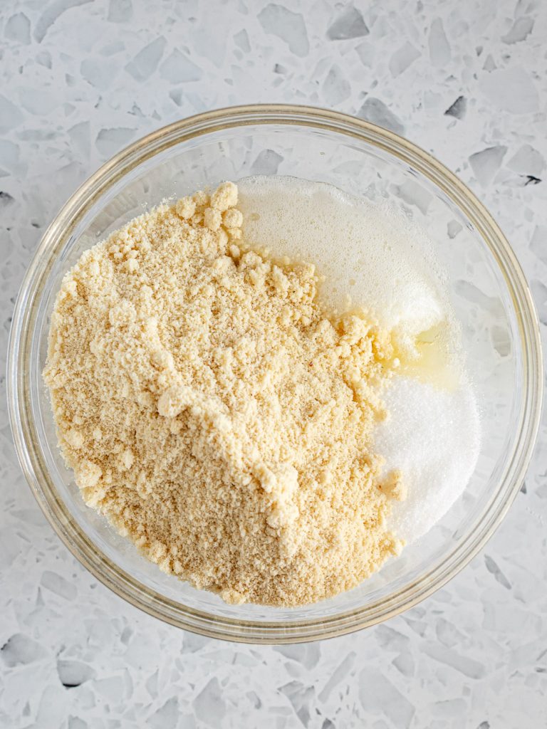 Almond meal, sugar and salt added to the frothy egg whites in a glass bowl, ready to be folded together.