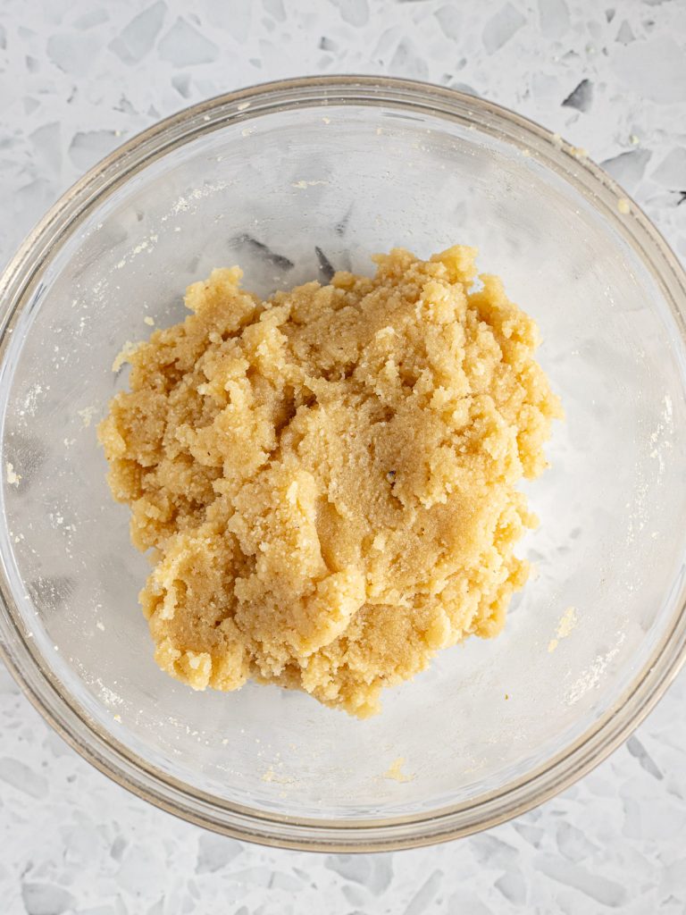 Rough, soft amaretti dough in a glass bowl, ready to be shaped into cookies.