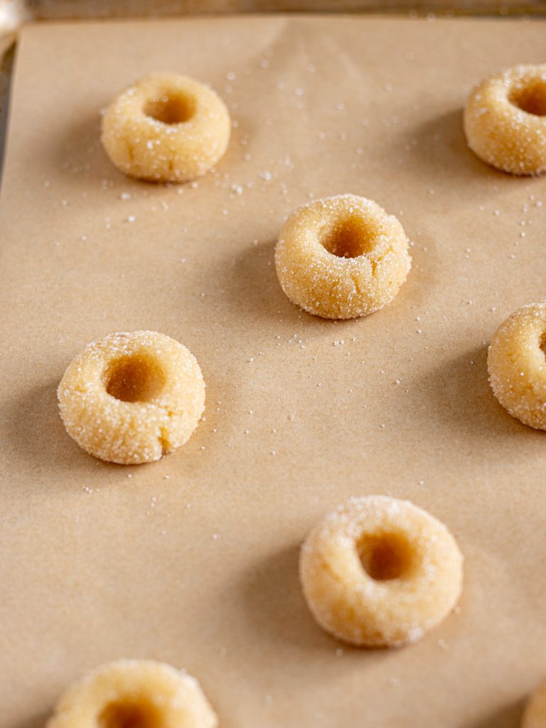 Shaped amaretti jam drop cookies arranged on a lined baking tray, ready to be chilled.