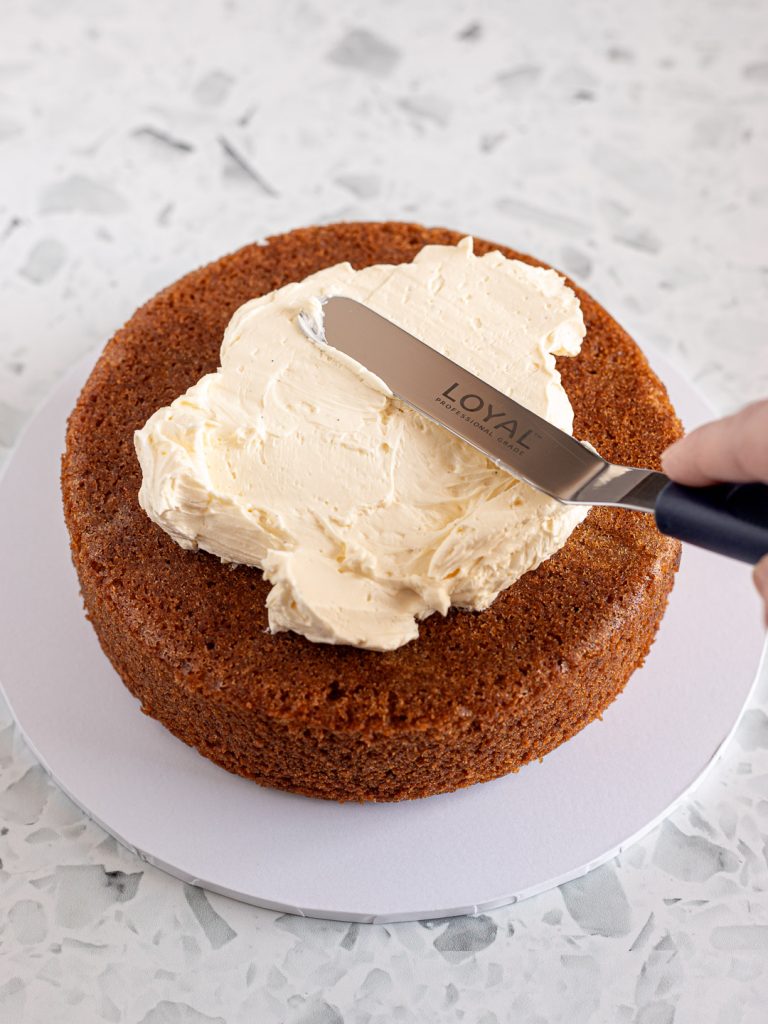 Vanilla Swiss meringue buttercream spread over the first cake layer on a cake board using an offset spatula.