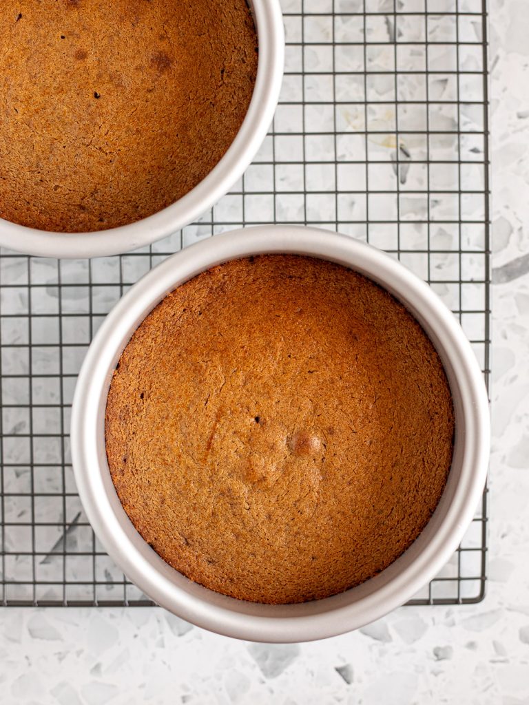 Two chai sponge cake layers cooling in light aluminium cake pans on a wire rack.