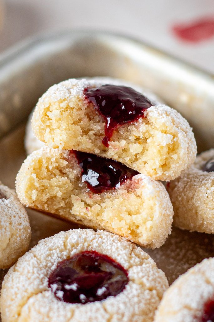 Close-up of two cherry amaretti jam drops with bites taken out, revealing their moist interiors and dark red cherry jam centres.