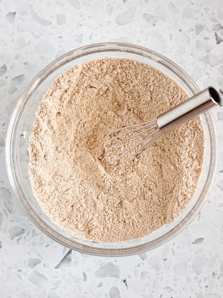 Dry ingredients combined in a glass bowl with a small whisk resting inside.