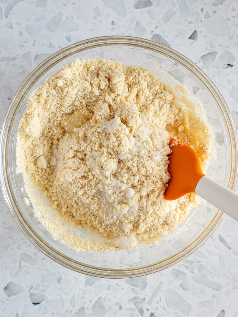 Dry ingredients being folded into the whisked egg whites with a rubber spatula to form a rough amaretti dough.