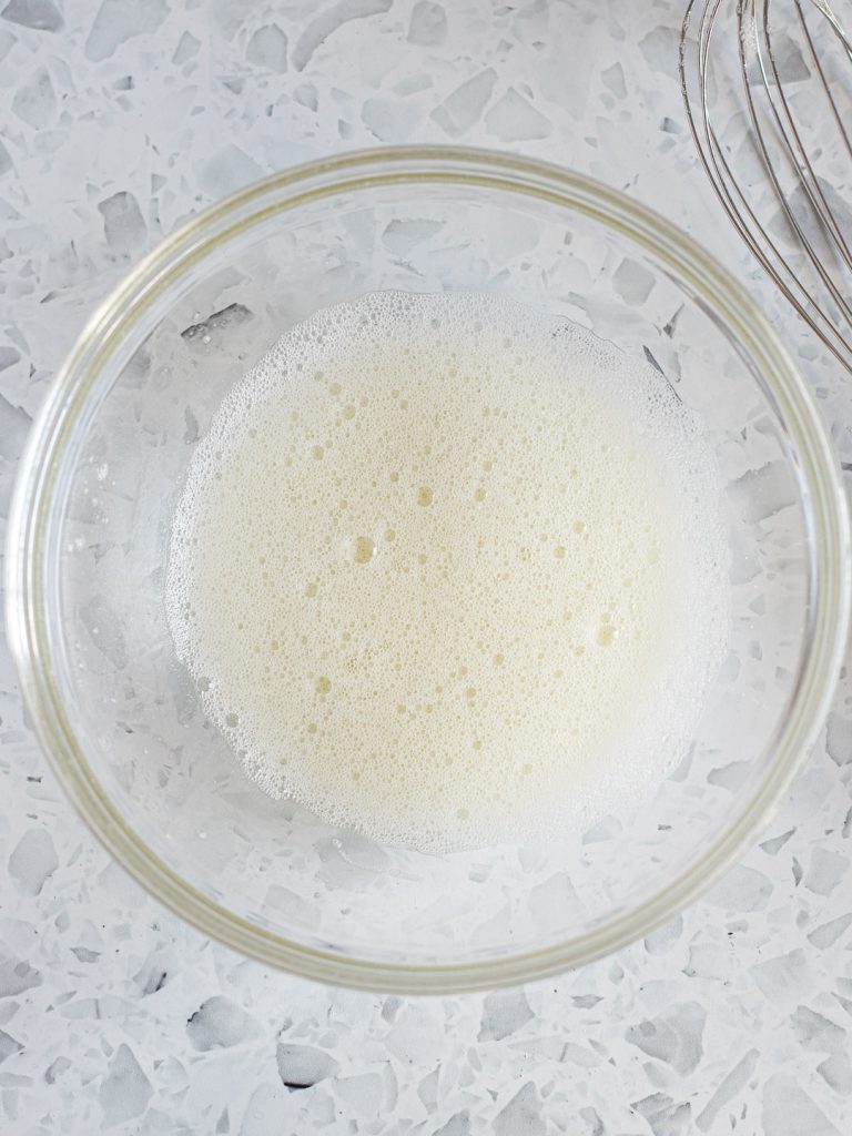 Egg whites whisked until frothy in a glass mixing bowl.